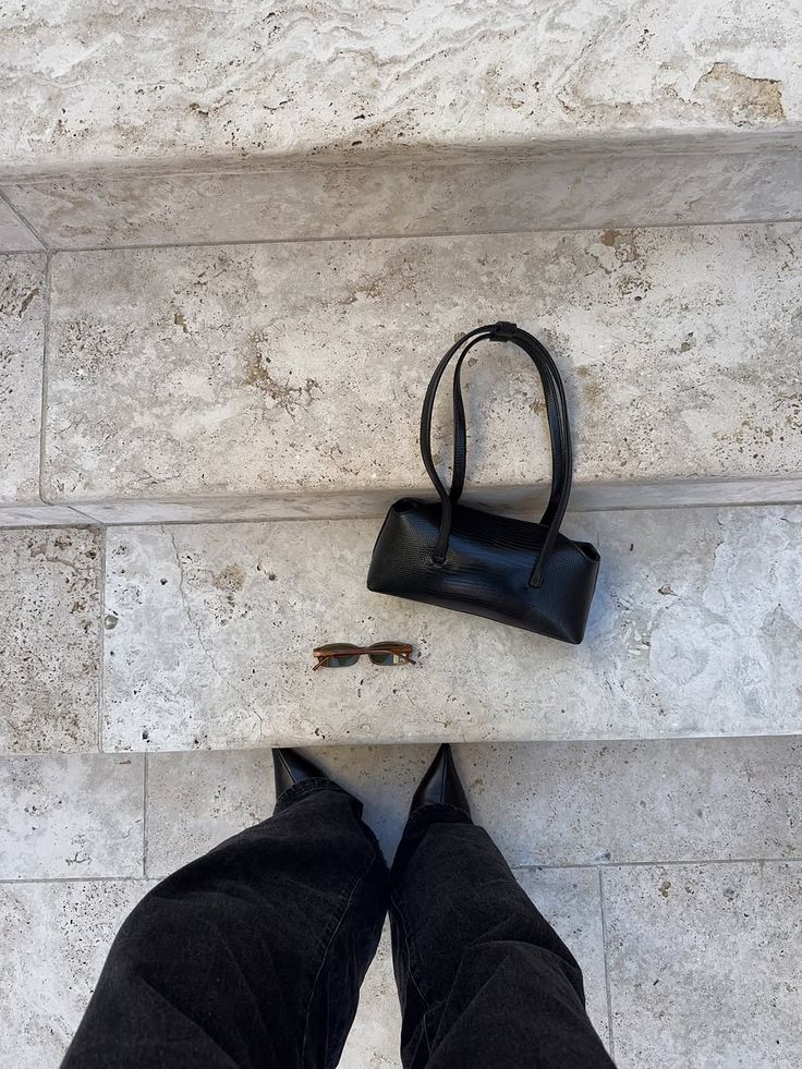 Black leather shoulder bag and sunglasses on travertine steps